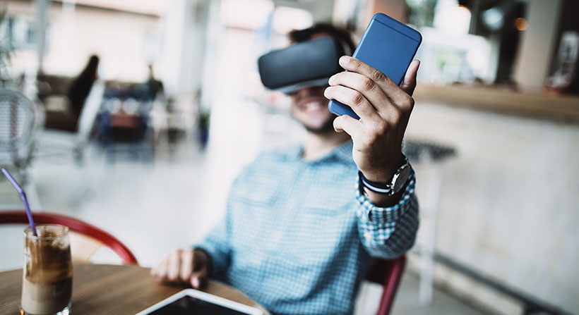 Young handsome man sitting in cyber cafe and using virtual reality headset or glasses