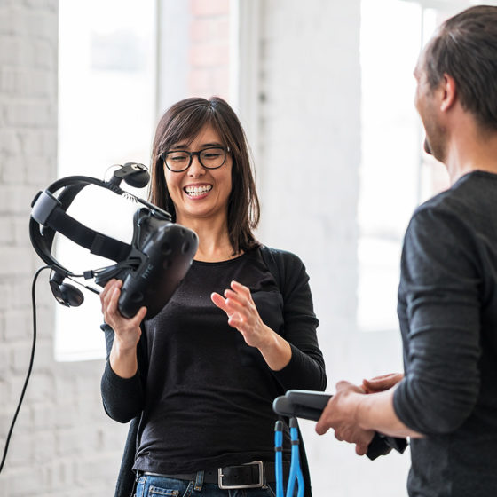 smiling female holding virtual reality headset and discussing with male engineer