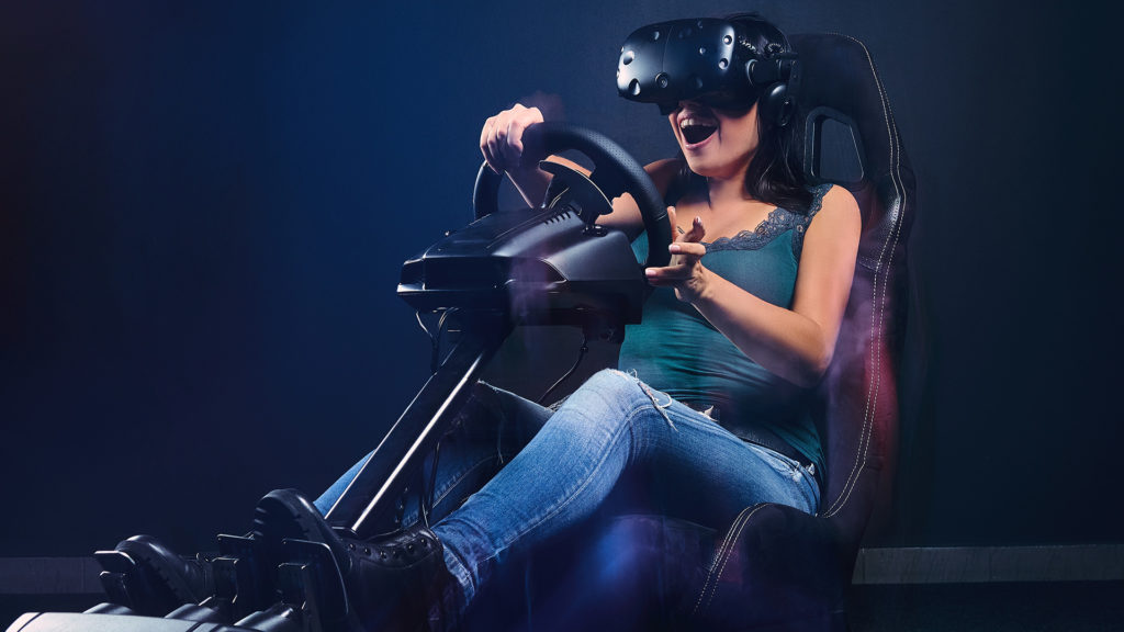 Woman wearing VR headset having fun while driving on car racing simulator cockpit with seat and wheel.