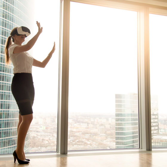 Excited businesswoman wearing headset experiencing real estate virtual tour standing near window