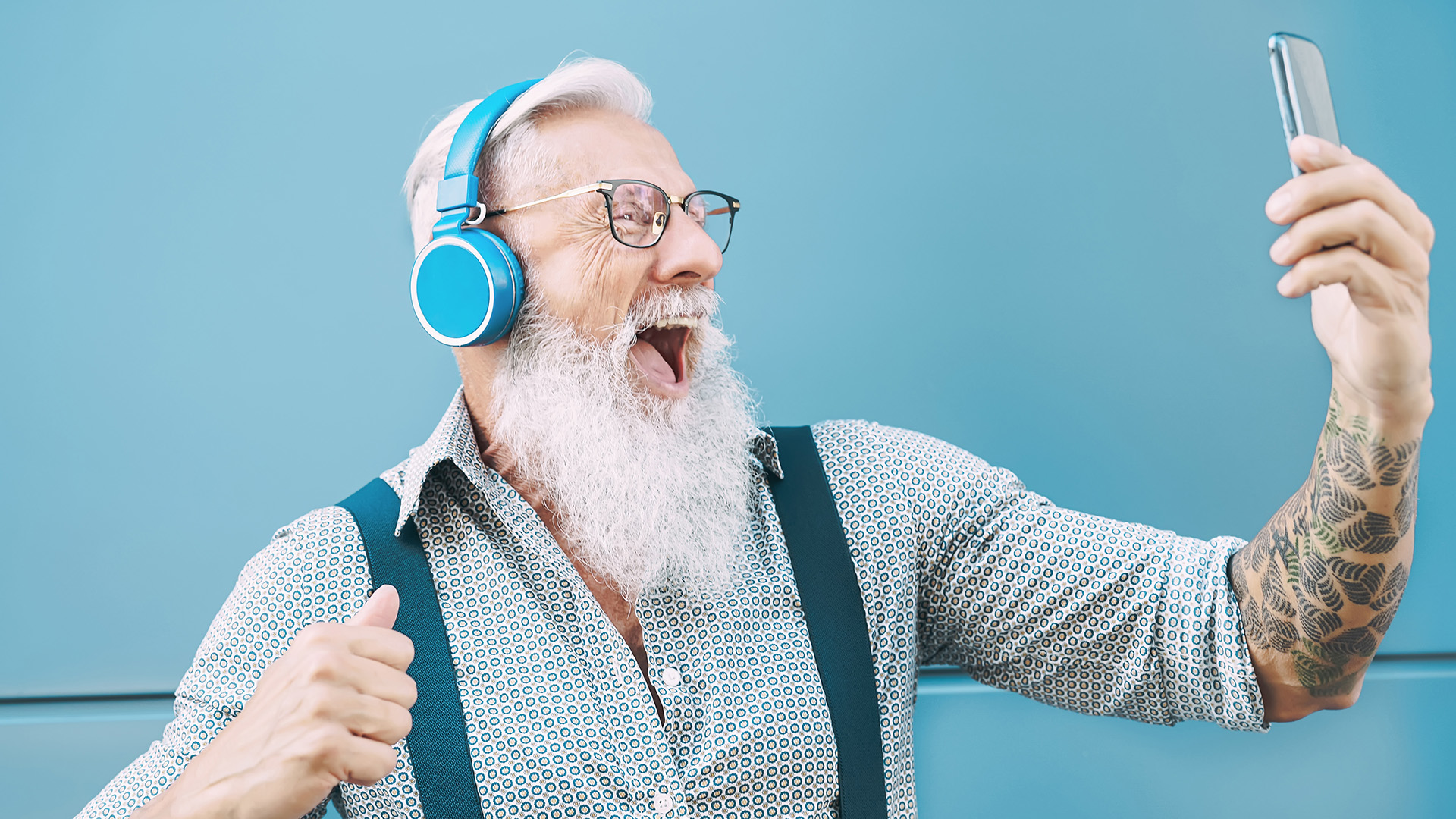 Happy senior male having fun using mobile smartphone playlist apps - technology and elderly lifestyle people concept for digital marketing