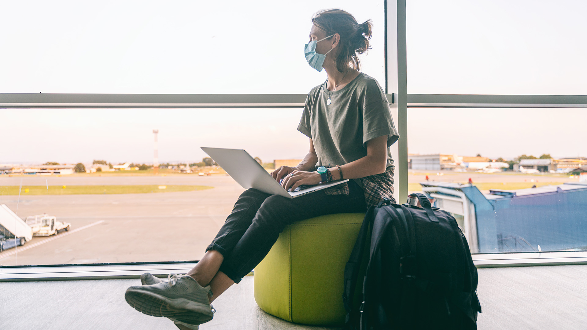 young digital nomad woman wearing a medical mask waiting for her plane at the airport in a post-pandemic world